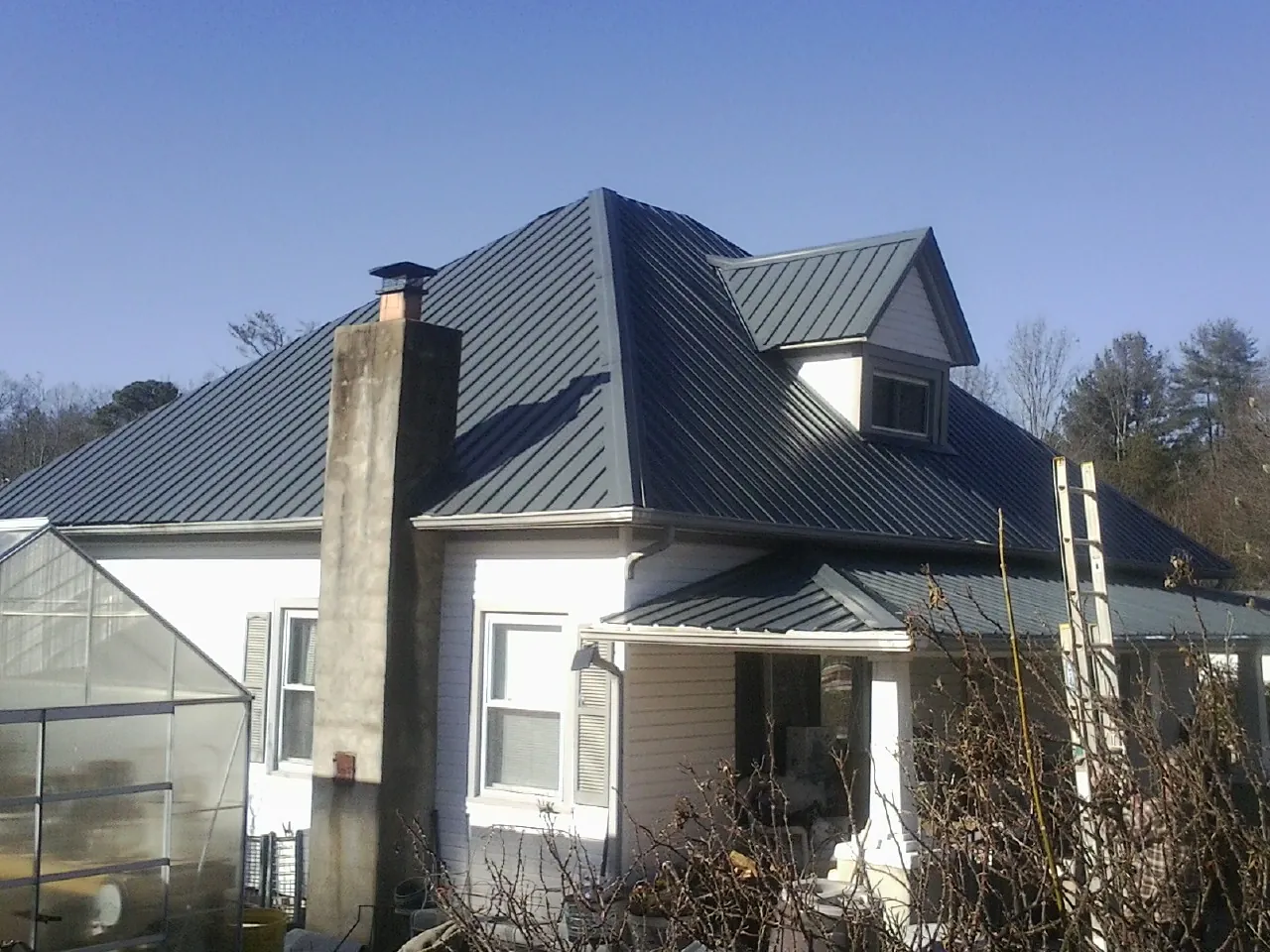 Dark blue standing seam metal roof on a white farmhouse with dormer — Slate & Tile Roof Repair by Roofing Brothers in Gasburg