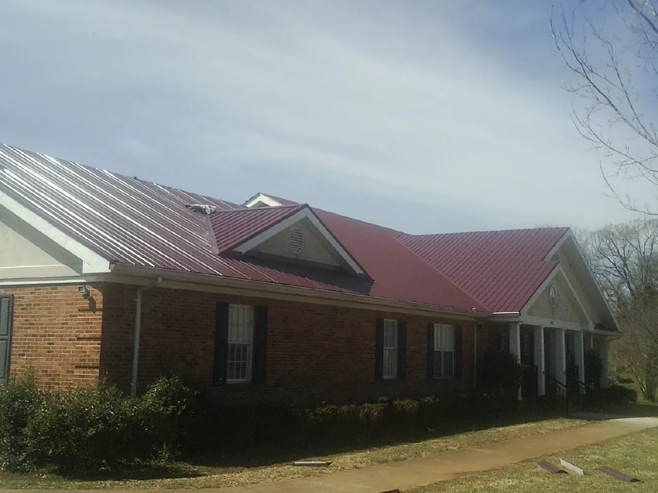 Red metal roof with gabled entries on a long brick building, from a Hail Damage Roof Repair job in Gasburg