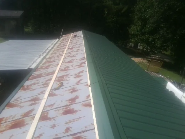 Old rusted panels beside newly installed green metal roofing — Wind Damage Roof Repair by Roofing Brothers in Gasburg