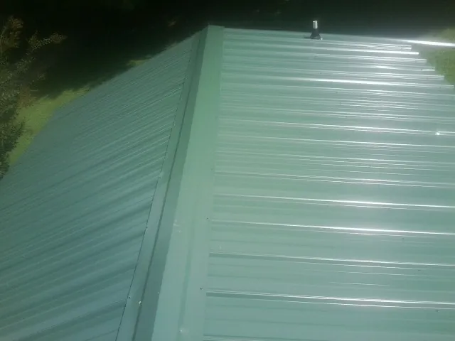 New green metal panels meeting at the ridge of a roof — Flat Roof Repair work by our crew in Gasburg
