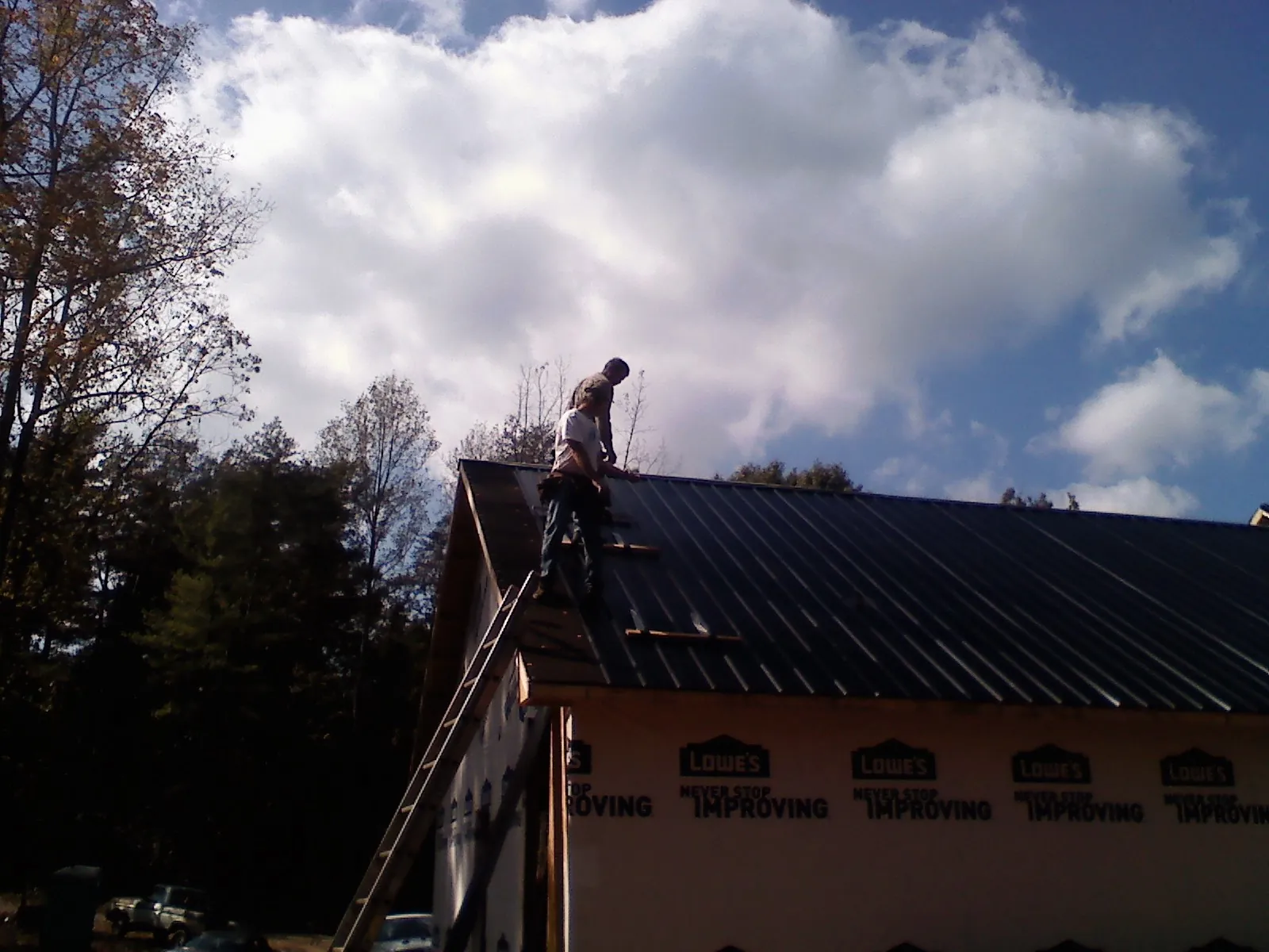 Roofer fastening dark metal panels high against a cloudy sky, from a Roof Inspection job in Gasburg