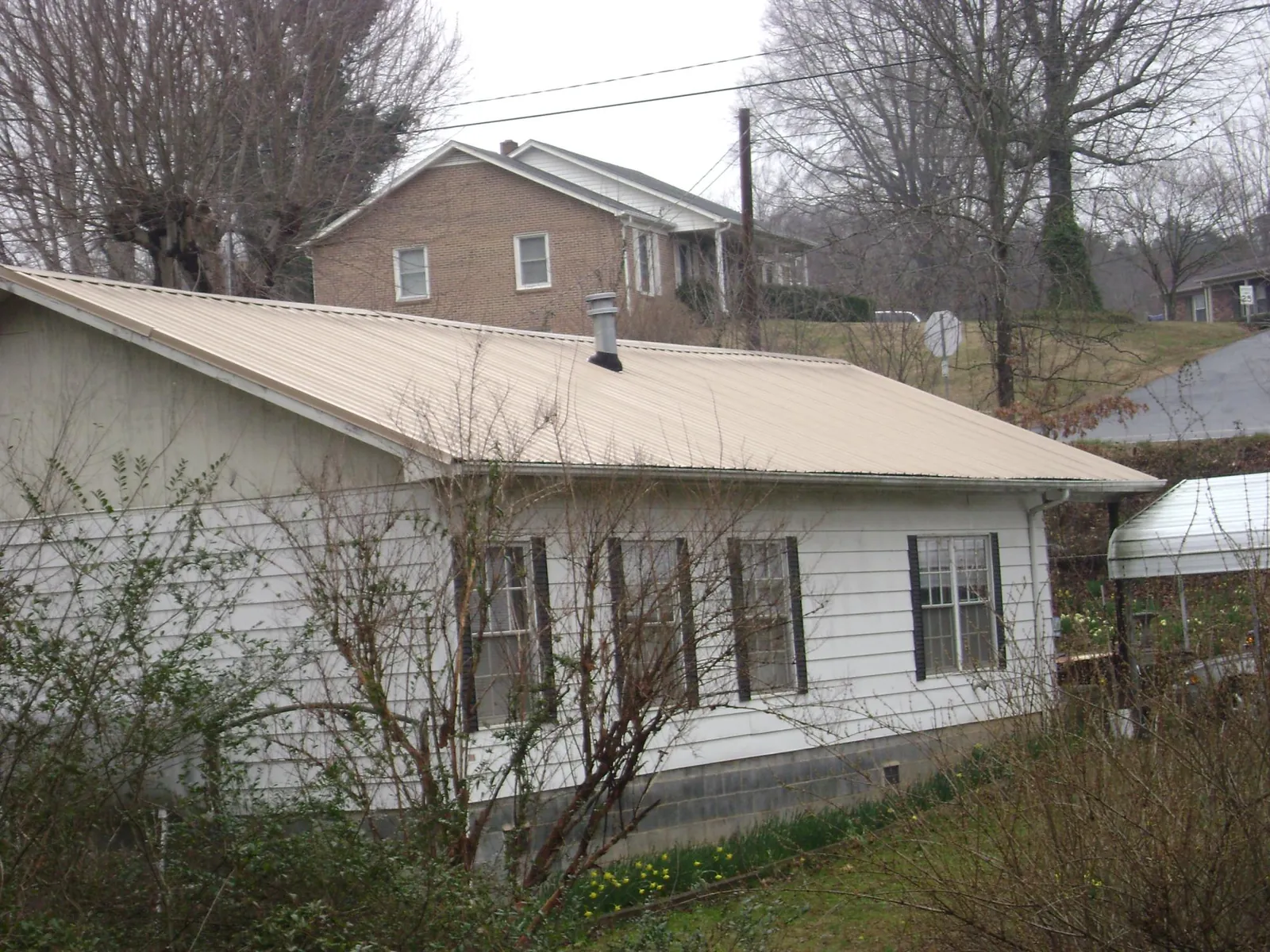 Tan metal roof on a white sided house set into a hillside — Commercial Roofing by Roofing Brothers in Gasburg